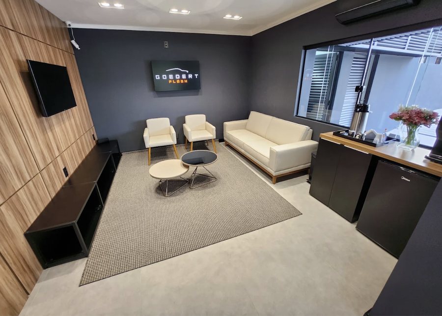 Sala de espera da loja, com sofá, poltronas e estação de café sob o letreiro da Goedert